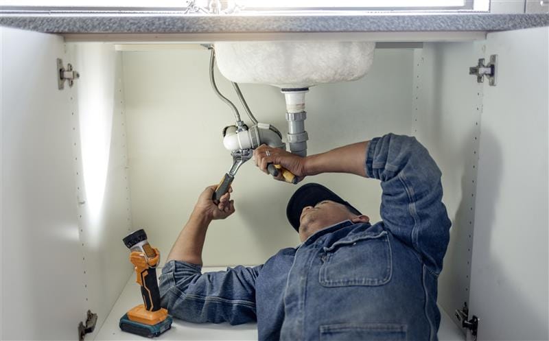 Plumber repairing pipes beneath a bathroom sink in Fleming Island