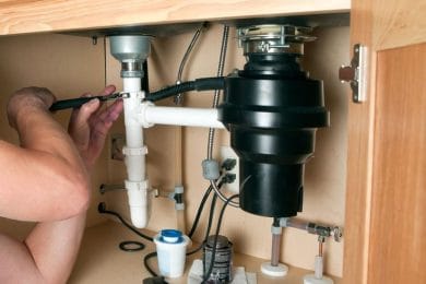 Plumber repairing a garbage disposal beneath a kitchen sink in Fleming Island