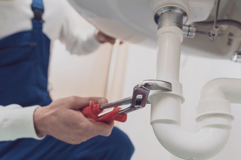 Plumber repairing a white drain pipe beneath a sink in Fleming Island